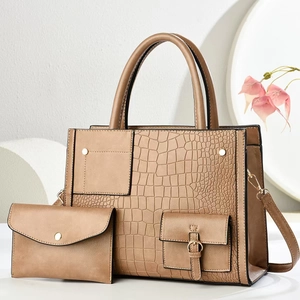 Close-up of brown crocodile embossed tote bag with matching envelope clutch on white stand
