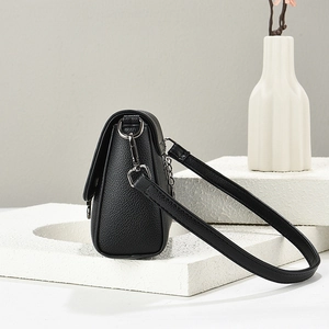 Detail of black lychee-grain PU leather crossbody bag with silver buckles on a white pedestal