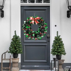Christmas wreath with red bow and berries on grey door between two small trees