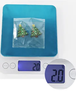 Close-up of glittery Christmas tree drop earrings with silver hooks on a weighing scale
