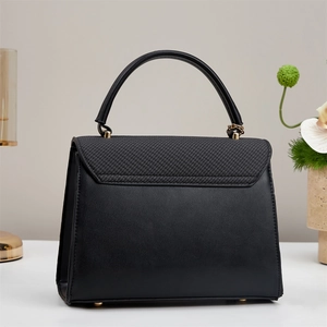 Detail of elegant black trapezoid handbag featuring mixed textures and gold hardware