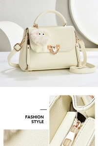 Close-up of white lychee pattern leather handbag with gold metal lock and plush charm