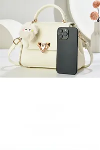 Detail view of large beige crossbody bag with metal lock and plush charm with phone for size