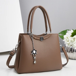 Detail of brown lychee grain leather tote bag with vintage metal badge and floral charm