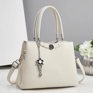 Close-up of beige lychee grain leather handbag with vintage buckle and floral pendant