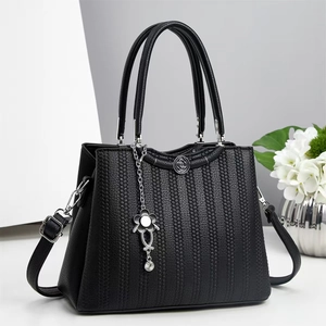 Detail of black tote bag with vertical pebble texture and floral silver pendant
