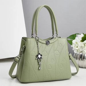Dettaglio borsa in pelle martellata verde chiaro con cuori goffrati e ciondolo a fiore