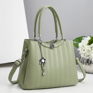 Close-up of sage green leather handbag with floral metal charm and textured finish