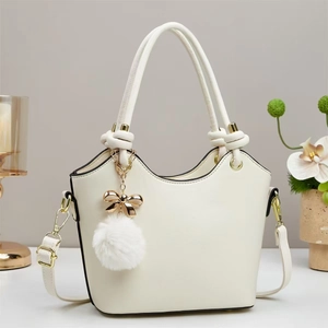 Detail of cream bucket bag showing wavy rim, golden bow, and soft plush ball charm