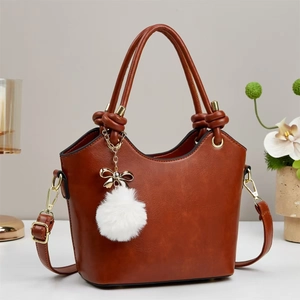 Caramel brown bucket bag with gold bow pendant and plush ball in a home setting