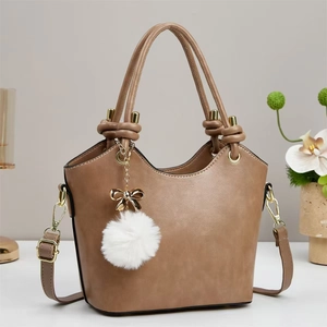 Close-up of khaki tote bag featuring gold hardware and a white plush pompom charm