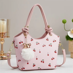 Borsa a secchiello rosa in pelle PU con stampe di ciliegie e ciondolo a pompon su tavolo