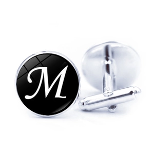 Detail of silver cufflinks with black round inlay and white floral letter M engraving