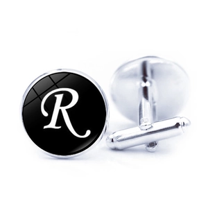 Detail of silver round cufflinks with black enamel and white letter R under glass dome