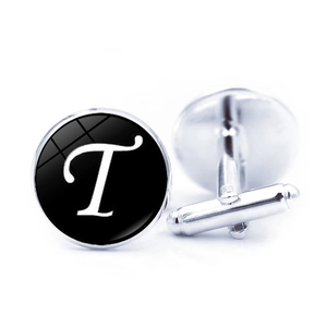 Macro detail of silver cufflink featuring a glass dome with a white letter T on black background