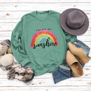 Flat lay of dark green sweatshirt with rainbow graphic and you are my sunshine lettering