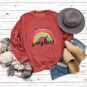 Detail of red sunshine rainbow sweatshirt styled with autumn accessories on white wood