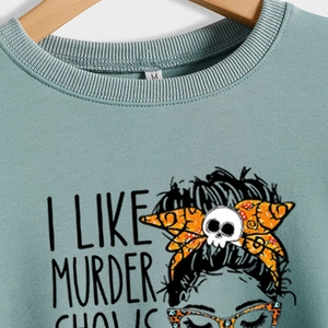 Green long sleeve shirt with skull graphic and I Like Murder Shows text on wooden hanger
