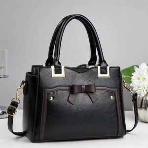 Detail of black lychee leather handbag with bow decor, gold hardware and metal bottom studs