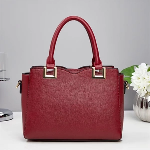 Detail of burgundy lychee pattern leather handbag with gold metal buckles and dual handles