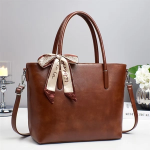 Detail of elegant caramel leather tote bag featuring a decorative silk scarf on the handle