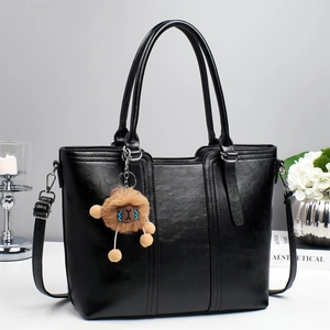 Detail shot of black tote bag with lychee texture and cute brown plush charm on white table