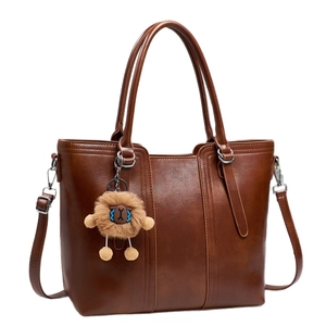 Dark brown faux leather tote bag with top handles and a plush lion charm on white background