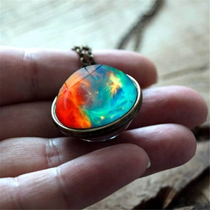 Handheld nebula galaxy glass ball pendant necklace with bronze chain on wooden background