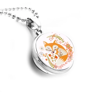 Macro detail of silver-tone round pendant featuring two orange foxes and floral art