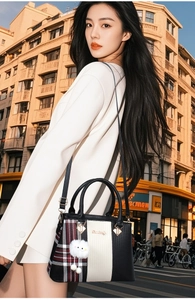 Detail of plaid tote bag with fur ball charm and gold hardware in city street setting