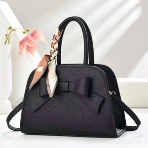 Detail of black pebbled leather handbag with large bow and fashion printed scarf handle