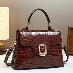 Detail of dark brown croc-embossed glossy leather handbag with gold oval metal buckle