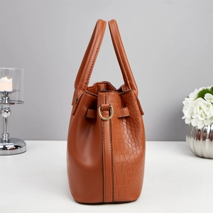 Detail view of brown handbag featuring crocodile texture and gold hardware accents