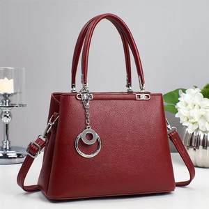 Close-up of a premium burgundy leather handbag with textured lychee grain and silver charm