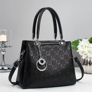 Detail of black textured handbag with embossed portrait design and silver chain charm