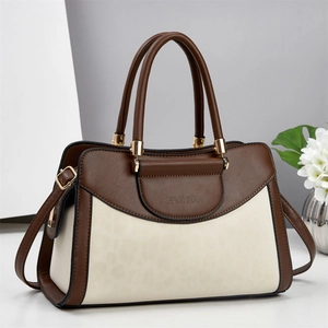 Brown leather and cream suede handbag with adjustable strap shown in a professional studio setting