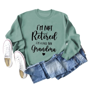 Flat lay of sage green sweatshirt with Grandma text, blue jeans and white shoes
