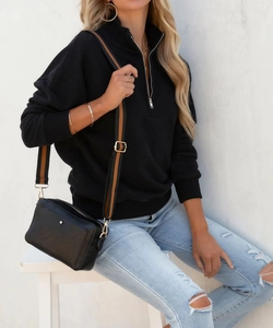 Felpa nera con mezza zip, jeans strappati e borsa a tracolla con cinturino a righe alla moda