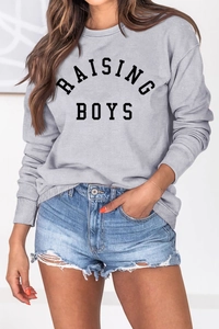 Close-up of the RAISING BOYS lettering on a gray crew neck sweatshirt with ribbed cuffs