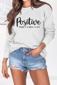 Détail de l'imprimé lettres Positive Mind vibes life sur sweat blanc à manches longues