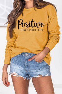Détail de l'imprimé Positive et des finitions côtelées sur le sweat-shirt moutarde