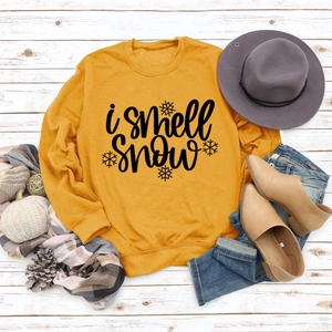 Flat lay of mustard yellow crewneck sweatshirt with i smell snow print and winter props