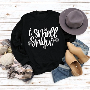 Flat lay of black crewneck sweatshirt with 'i smell snow' text and winter props
