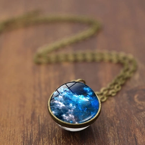 Vintage double-sided glass galaxy pendant necklace with blue nebula on wooden background