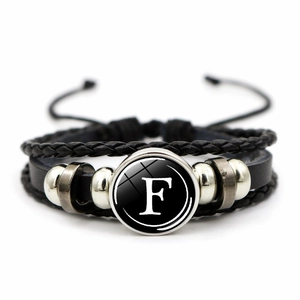 Macro detail of multi-layer woven leather bracelet featuring black letter F glass charm