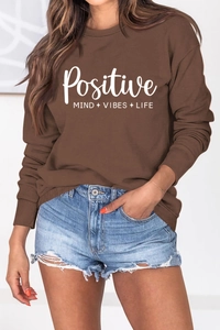 Gros plan du lettrage Positive Mind Vibes Life sur un sweat-shirt marron à manches