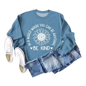 Flat lay of blue sweatshirt featuring sunflower print and Be Kind slogan with jeans
