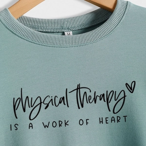 Sage green Physical Therapy sweatshirt with heart letter print on wooden hanger