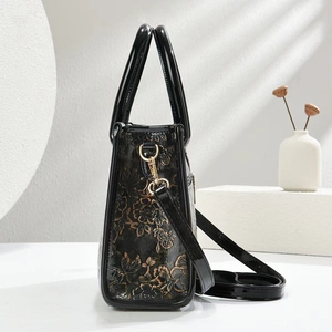 Detail of black patent leather tote bag with 3D embossed bronze floral pattern and gold hooks