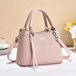 Detailed view of pink woven texture handbag with fringe tassel and adjustable shoulder strap